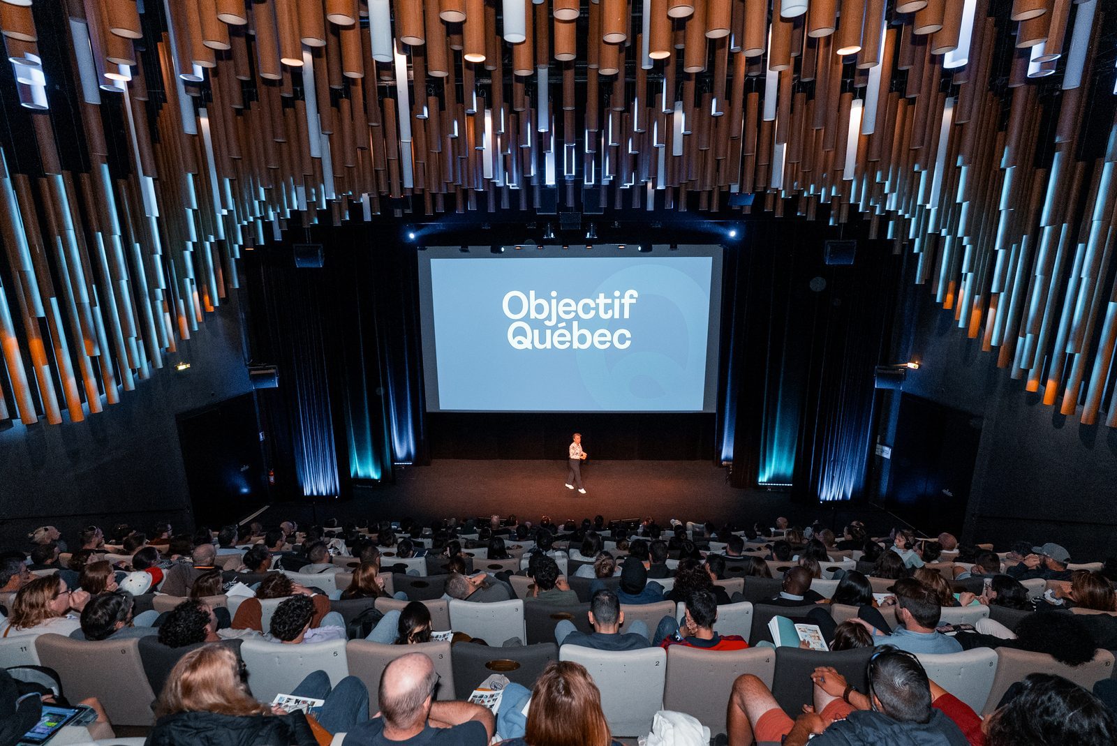 La salle de cinéma pleine pendant la conférence d'Objectif Québec, avec le logo sur grand écran